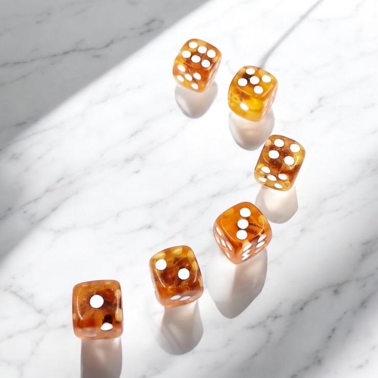 Close-up macro image of a handcrafted Baltic amber playing die, revealing detailed natural inclusions and organic texture within the gemstone.